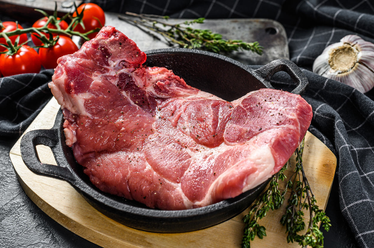 Raw pork cutlet steak in a pan. Piece of raw meat ready for preparation with greens and spices.  Black background. Top view.